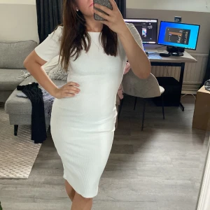 Vit ribbad klänning i midilängd - Säljer en vit ribbad klänning med korta ärmar och rund halsringning. Klänningen har en kroppsnära passform och är tillverkad i ett stretchigt material som sitter snyggt på kroppen. Kan användas som studentklänning 🤍🤍🎓