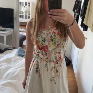 Blommig sommarklänning från Oasis - Säljer en superfin blommig klänning från Oasis i vitt med färgglada blommor. Klänningen är ärmlös med knytband på axlarna och har en avslappnad passform. Perfekt för varma dagar och midsommarfirande!