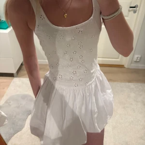 Vit klänning med broderade blommor - Superfin vit klänning med ganska breda axelband och broderade blommor på överdelen. Kjolen är luftig och har en kort längd, perfekt för varma dagar. Söt och somrig stil som passar till många tillfällen. Säljer då den inte passade riktigt 