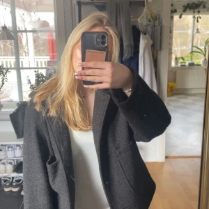 Svart kappa från 157 - Säljer en svart kavaj från lager 157 i klassisk modell med krage och två stora fickor framtill. Jackan är fodrad och har knappar vid ärmslut och framtill. Perfekt för dig som gillar en stilren look.