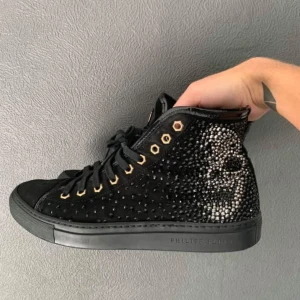  Philipp Plein skor, in store exclusive - Säljer ett par svarta Philipp Plein sneakers med glittrande döskallemotiv på sidorna och små nitar över hela skon. Skorna har svarta snören, guldfärgade öljetter och platt sula. Märkesdetalj på plösen och insida i skinn. Står 39 på insidan av läppen men storleken är mer egentligen 40,5. Har tyvärr varken  kvitto eller box. Köpt in store i Italien för 7000, mitt pris 1000. Bvsa 