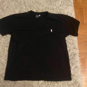 Svart t-shirt från Polo Ralph Lauren - Klassisk svart t-shirt från Polo Ralph Lauren med liten broderad logga på bröstet. T-shirten har rund halsringning och korta ärmar. Perfekt basplagg med stilren design. använd 2 gånger