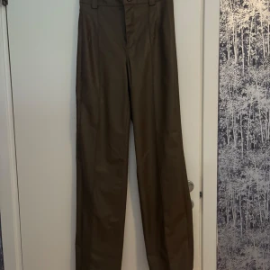 Bruna skinnbyxor med raka ben - Säljer ett par bruna byxor i skinnimitation med raka ben och hög midja. Byxorna har bälteshällor och klassisk passform, perfekta för att lyfta vilken outfit som helst.