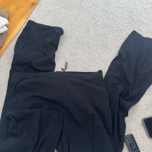 Svarta mjukisbyxor med dragsko - Svarta mjukisbyxor med avslappnad passform och dragsko i midjan. Perfekta för en chill dag hemma eller när du vill vara bekväm. Byxorna har raka ben och är gjorda i ett mjukt material.