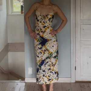 Mönstrad långklänning med tunna axelband - Säljer en långklänning med tunna axelband och knyt framtill samt öppen rygg. Modellen är figurnära och har en feminin siluett, perfekt för varma dagar.☀️