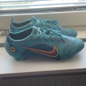 Turkosa Nike Mercurial vapor 14 elite fg - Säljer ett par turkosa Nike Mercurial fotbollsskor med färgglad Swoosh i rött och gult. Skorna har snörning och platt sula med dobbar för gräsplan ända nackdelen är att en dobb på vänsterskon har blivit kortare men det är inget som  känns på plan eller vid användning  . Lätta och smidiga för snabba rörelser på planen. Priset är inte hugget i sten så är öppen för prisförslag och tveka inte att höra av sig vid minsta lilla.