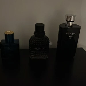Parfymset med Valentino och Prada - Säljer två exklusiva herrparfymer: Valentino i en mörk, mönstrad flaska och Prada i en elegant svart flaska med silverdetaljer. Perfekta för dig som gillar lyxiga och stilrena dofter.
