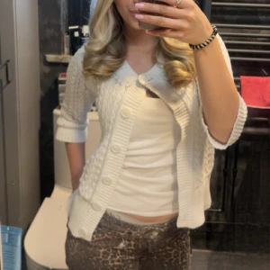 Vit stickad kofta med knappar - Säljer en söt vit stickad kofta med stora knappar och ribbade detaljer. Koftan har kort ärm och ett klassiskt kabelstickat mönster. Helt slutsåld köpt för 500kr