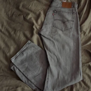 Grå jeansbyxor från Levi's 551 - Säljer ett par grå Levi's 551 jeans med klassisk femficksdesign och raka ben. Byxorna har läderpatch bak i midjan och tydliga sömmar. Perfekta för dig som gillar en tidlös och avslappnad stil.