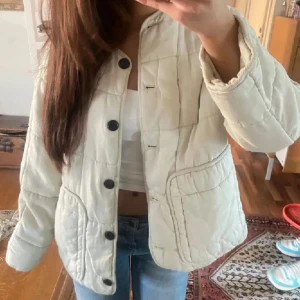 Superfin quiltad jacka från Zara - Säljer en beige quiltad jacka med svarta knappar och stora fickor framtill. Jättemysig o kön att ha på våren/sommaren (:.