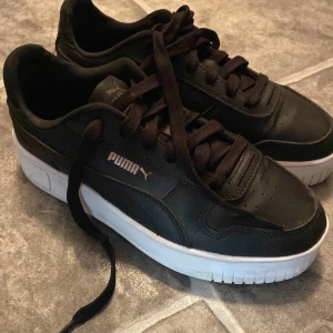 Svarta sneakers från Puma - Säljer ett par svarta Puma sneakers med vit, tjock sula och klassisk snörning. Skorna har rund tå och Puma-logga på sidan samt på sulan. 