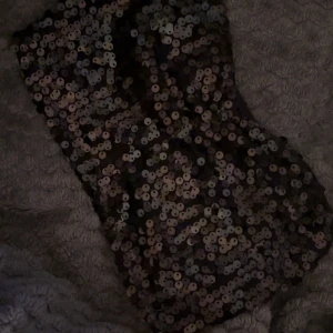 Svart paljett-tubtopp - Säljer en svart tubtopp täckt med glittrande paljetter. Perfekt för dig som vill sticka ut och glänsa lite extra. Toppen är axelbandslös och har en figurnära passform.