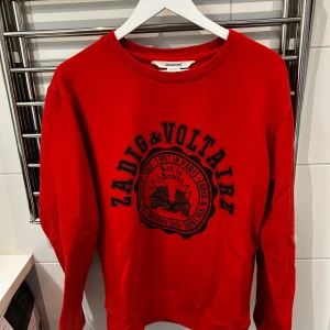 Röd sweatshirt från Zadig & Voltaire - Röd sweatshirt med svart tryck framtill från Zadig & Voltaire. Rund halsringning och långa ärmar.