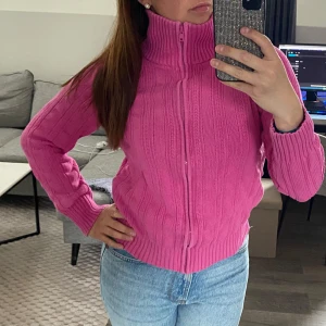 Rosa stickad kofta med dragkedja - Säljer en rosa stickad kofta med hög krage och dragkedja framtill. Tröjan har långa ärmar och ribbade muddar vid ärmslut och nederkant. 