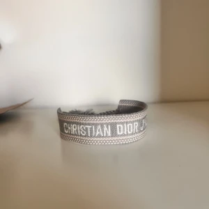 Grått armband från Christian Dior - Snyggt grått armband från Christian Dior med vävd logotyp och justerbar knytning. Perfekt accessoar för att lyfta din stil med en lyxig touch.