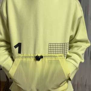 Gul hoodie med rutmönster och dragsko - Snygg ljusgul hoodie med svart rutmönster och siffran 1 framtill. Stor känguruficka med dragsko och luva. Perfekt för en avslappnad stil. Ny och knappt använd