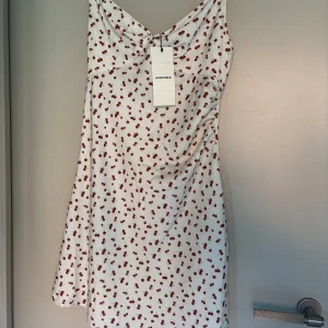 Vit klänning med körsbärsmönster från Adoore oanvänd med prislapp - Supersöt vit klänning från Adoore med röda körsbär över hela tyget. Klänningen har smala axelband, lätt rynk vid bysten och en feminin, figurnära passform. Perfekt för sommaren!!