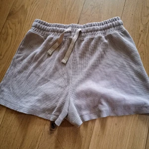 Beige ribbade shorts från H&M - Säljer ett par ljusbeige shorts från H&M i ribbat bomullstyg. Quiltat. Rutigt. De har resår i midjan och dragsko för justerbar passform. Perfekta för en avslappnad stil under varma dagar. 65% polyester 35% bomull. Ytludd finns som materialet snabbt fick. Använda enstaka gång 