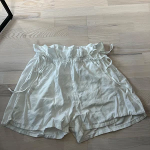 Vita shorts med knyt från Chiquelle - Säljer ett par vita shorts från Chiquelle i storlek large. De har hög midja med volangkant och knytband i midjan. Materialet känns lätt och luftigt, perfekt för varma dagar.