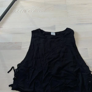 Svart blus med snörning från Gina Tricot - Svart blus från Gina Tricot i storlek 38. Blusen har snörningsdetaljer på sidorna som ger en söt look. 