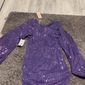 Lila glittrig omlottklänning från Bubbleroom - Säljer en lila glittrig omlottklänning från Bubbleroom med långa puffärmar och figurnära passform. Klänningen har v-ringning och är täckt av paljetter som ger ett riktigt festligt intryck. Perfekt för dig som vill sticka ut!