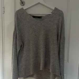 Grå stickad tröja från Vero Moda - Mysig grå stickad tröja från Vero Moda med avslappnad passform och rund halsringning. Perfekt för lager-på-lager och passar till både jeans och kjol. Långa ärmar och ribbad struktur ger en stilren look.
