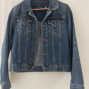 Klassisk blå jeansjacka från Earl Jean - Säljer en klassisk blå jeansjacka från Earl Jean i storlek S. Jackan har knappar framtill, två bröstfickor med lock och långa ärmar. Perfekt att slänga över en t-shirt eller hoodie för en avslappnad look.