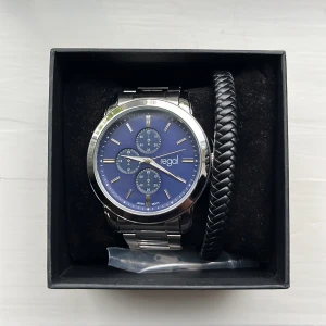 Regal herrklocka med blå urtavla  - Stilren herrklocka från Regal med blå urtavla, silverfärgat länkarmband i metall och flera små urtavlor. Klockan levereras i originalask tillsammans med ett svart flätat armband. Det finns fler länkar om man vill förstora den. 