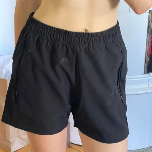 Svarta träningsshorts från Endurance - Svarta träningsshorts från Endurance med elastisk midja och dragkedjefickor på sidorna. Perfekta för löpning eller gym men tyvärr lite stora för mig.