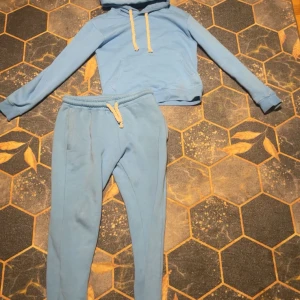 Ljusblå hoodie och en blå syna world byxa - Ljusblå hoodie med vit snörning och coolt graffiti-tryck på huvan. Tröjan har känguruficka och långa ärmar. Perfekt för dig som gillar streetstyle och vill ha en chill look. Matchande byxor ingår i annonsen