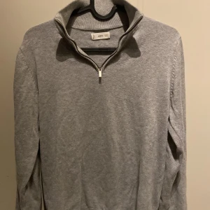 Grå half zip tröja från MNG - Snygg grå långärmad tröja från MNG med half zip-dragkedja och hög krage. Tröjan är i mjuk bomullsmix och har en clean, stilren look som passar perfekt till jeans eller kjol. Enkel att matcha och superbekväm för kyligare dagar.