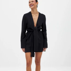 Svart omlottklänning med knyt - Snygg svart kortklänning med omlott och knyt framtill. Djup v-ringning och långa ärmar. Klänningen har en avslappnad passform och är gjord i ett mjukt, strukturerat tyg. Klänningen är helt ny och aldrig använd, lapp finns kvar. Nypris 349kr. 