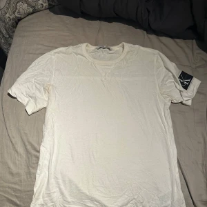 Vit t-shirt från Calvin Klein Jeans - Vit t-shirt från Calvin Klein Jeans i mjuk bomull. Klassisk rund halsringning och korta ärmar. På vänster ärm sitter en svart patch med CK-loggan. Enkel och clean design som passar till allt.väldigt sällsynt tröja