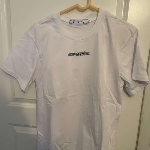 Vit Off-White t-shirt med röd print - Snygg vit t-shirt från Off-White med klassisk logga framtill och stor röd grafisk print på ryggen. T-shirten har rund hals och korta ärmar, perfekt för en clean streetwear-look. Materialet är mjuk bomull som känns skönt mot huden.