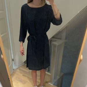 Mörkblå prickig klänning Bondelid - Mörkblå kortklänning från Bondelid med vita prickar, trekvartsärm och knytband i midjan. Snygg och avslappnad passform. Är i storlek 42, men passar fler storlekar då det är knytband i midjan. Jag har storlek 36/38 på bilden. 