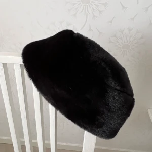 Svart pälsmössa i klassisk modell - Mysig svart pälsmössa (ej äkta) med rundad form och fluffig yta. Perfekt för kalla dagar när du vill hålla värmen och samtidigt se stilren ut. Passar dig som gillar en tidlös och elegant look. Ny utan prislapp 
