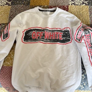 Vit sweatshirt från Off White med tryck - Vit sweatshirt från Off White med stora svarta och röda tryck på både fram- och baksida samt ärmarna. Tröjan har rund halsringning och ribbade muddar. Snygg streetwear-stil med tydlig logga och grafiska detaljer.