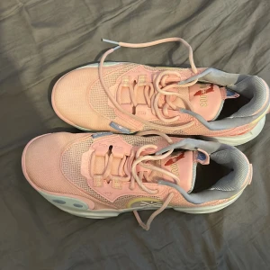 Way of Wades All city sunshine state  - Säljer ett par rosa sneakers från Li-Ning med meshdetaljer och snörning. Skorna har vita och ljusblå inslag samt unikt mönstrad häl i rött och vitt. Sulan är mönstrad i grått och gult. Perfekta för dig som gillar färgglada och sportiga skor.