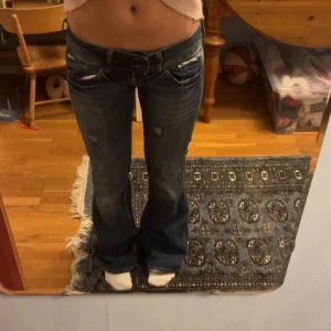 jätte lågmidjade byxor - Säljer ett par mörkblå jeans med bootcut passform och slitna detaljer framtill. Jeansen har låg midja och klassiska fem fickor. Perfekta för dig som gillar en retro vibe och vill ha ett par snygga jeans med lite extra attityd.