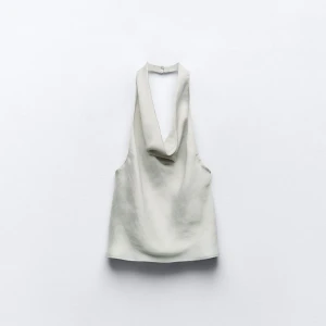 Silvrig/grå halterneck topp från Zara - Säljer en stilren vit halterneck topp från Zara med snygg draperad urringning. Toppen har en slät, lätt glansig yta och är ärmlös med öppen rygg. Perfekt för dig som gillar minimalistisk och trendig stil. Aldrig använt och prislapp kvar! Skriv för fler bilder!🫶💕