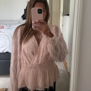 Ljusrosa fluffig blus från Vila - Supersöt ljusrosa blus från Vila med fluffiga detaljer och v-ringning. Blusen har långa ärmar, omlott-effekt och smock i midjan för en snygg siluett. Perfekt för dig som vill sticka ut med en unik och trendig topp! Använd 1 gång!💓