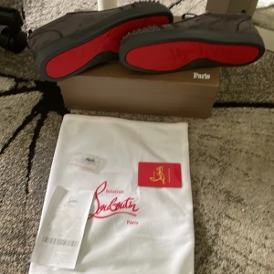 Christian Louboutin sneakers med röd sula - Snygga svarta sneakers från Christian Louboutin med ikonisk röd sula. Skorna har en stilren design med rund tå och snörning, tillverkade i skinn. Perfekta för dig som vill sticka ut med exklusiva detaljer och lyxig känsla.