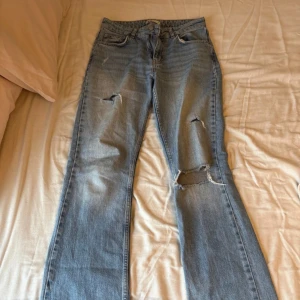 Ljusblå slitna jeans med raka ben - Säljer ett par ljusblå jeans med flera slitningar och hål på benen. Jeansen har klassisk femficksdesign, normal passform och raka ben. Perfekta för en avslappnad och trendig look. Nypris 599