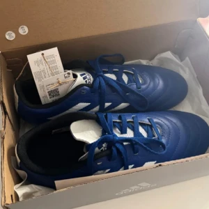 Adidas fotbollsskor - Snygga blå adidas Copa fotbollsskor med klassiska vita ränder och snörning. Skorna har en rund tå. 