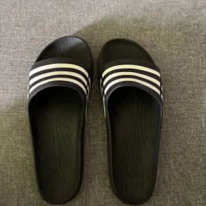 Svarta Adidas tofflor - Klassiska svarta tofflor från Adidas. Perfekta att slänga på sig till stranden eller efter träningen.