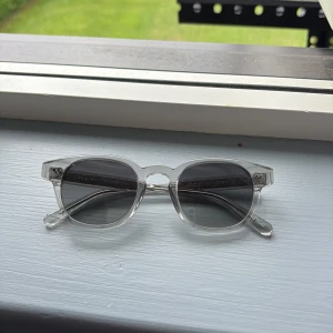 Gråa Chimi 01’or - Snygga solglasögon med transparent båge och gråtonade glas. Modern och stilren design som passar till alla outfits. Bågarna är lätta och bekväma. Perfekta för sommaren och stranden.