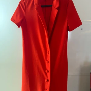 Röd kort klänning från Zara - Snygg röd klänning från Zara med korta ärmar och klassisk krage. Klänningen har knappar framtill och en rak, enkel passform som ger en stilren look. Perfekt för dig som vill sticka ut med färg och enkelhet.