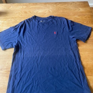 Marinblå t-shirt från Polo Ralph Lauren - Snygg marinblå t-shirt från Polo Ralph Lauren med klassisk röd broderad logga på bröstet. T-shirten är i 100% bomull och har en normal passform med korta ärmar. Perfekt för dig som gillar stilrena och tidlösa plagg.