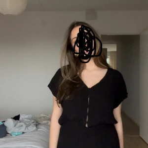 Svart kort jumpsuit med knappar - Supersöt svart kort jumpsuit med v-ringning, knappar framtill och resår i midjan.  Perfekt för att ta med till stranden 🖤Storlek L