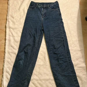 Mörkblå raka jeans med hög midja - Säljer ett par mörkblå jeans med klassisk rak passform och hög midja. Jeansen har fem fickor, bälteshällor och stängs med dragkedja och saknar knapp. Perfekta för en chill och stilren look.